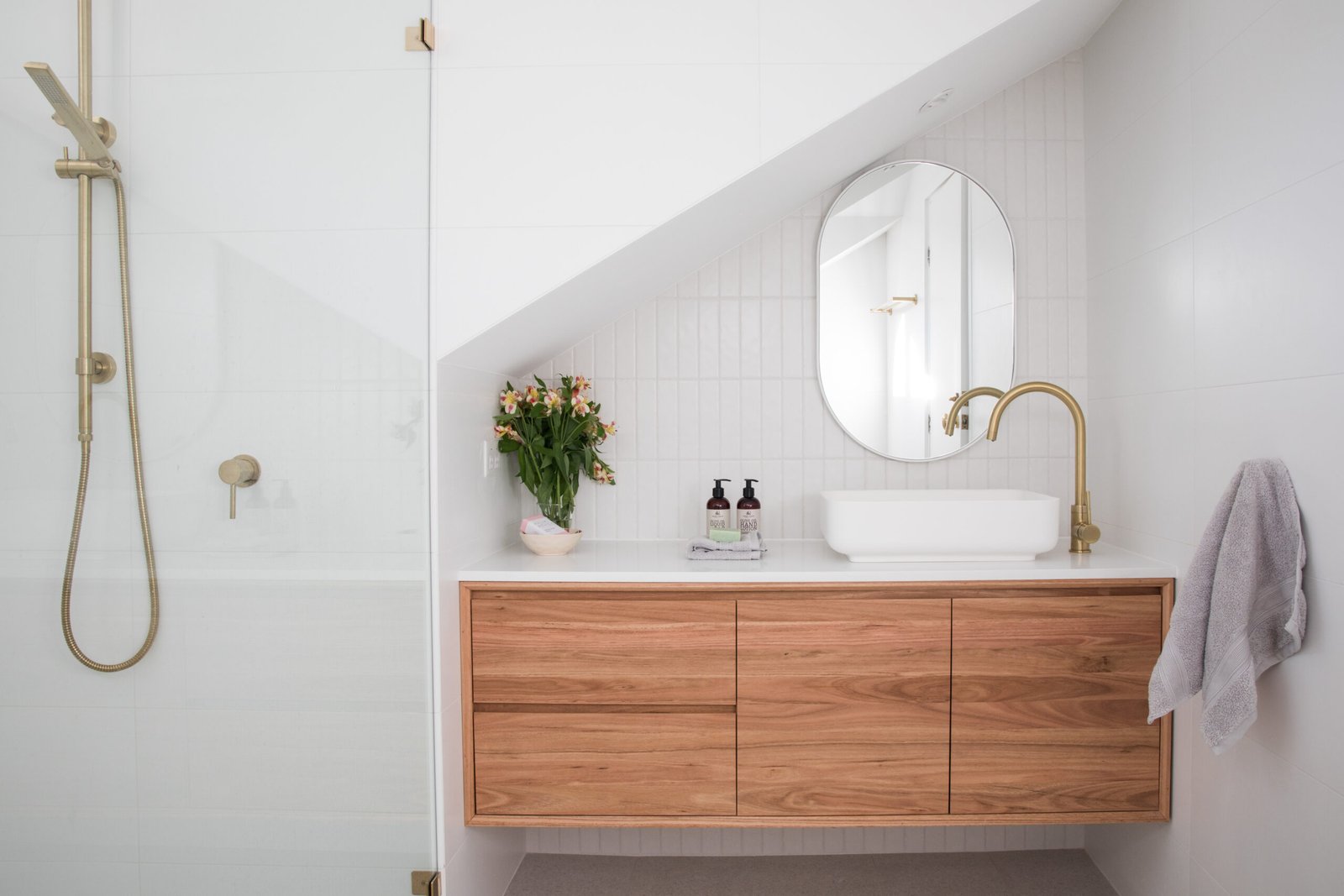 Modern roof attic bathroom timber stone benchtop vanity gold brass tap white basin small space slanted roof tiled wall elegant natural light renovation new